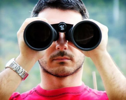 A young man peers through binoculars. (photo © gerlos via the Flickr Creative Commons)