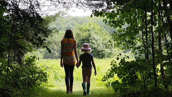 Two girls walk hand in hand from the woods into the field at the Fremont Conservation Land in Peterborough. (photo © Francie Von Mertens)