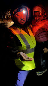 A man holds a small child in his left arm, while holding a spring peeper in his right. Both he and the child are looking down at the peeper, and bathed in red light from a headlamp. (photo © Chandra Balakrishna)