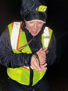 A woman in a reflective vest and raingear smiles while holding a spotted salamander. (photo © Sarah Thomas)