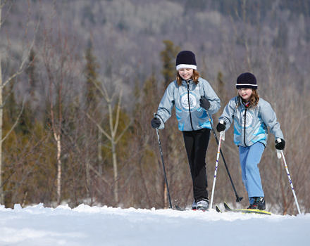 Two children cross-country ski through an open field, with woods in the distance. (photo © Province of British Columbia via the Flickr Creative Commons)
