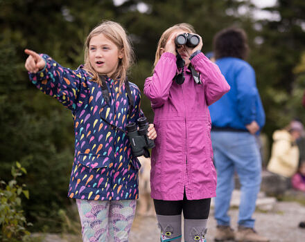 Two girls watch for hawks, one pointing and one using binoculars. (photo © Ben Conant)
