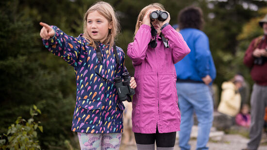 Two girls watch for hawks, one pointing and one using binoculars. (photo © Ben Conant)