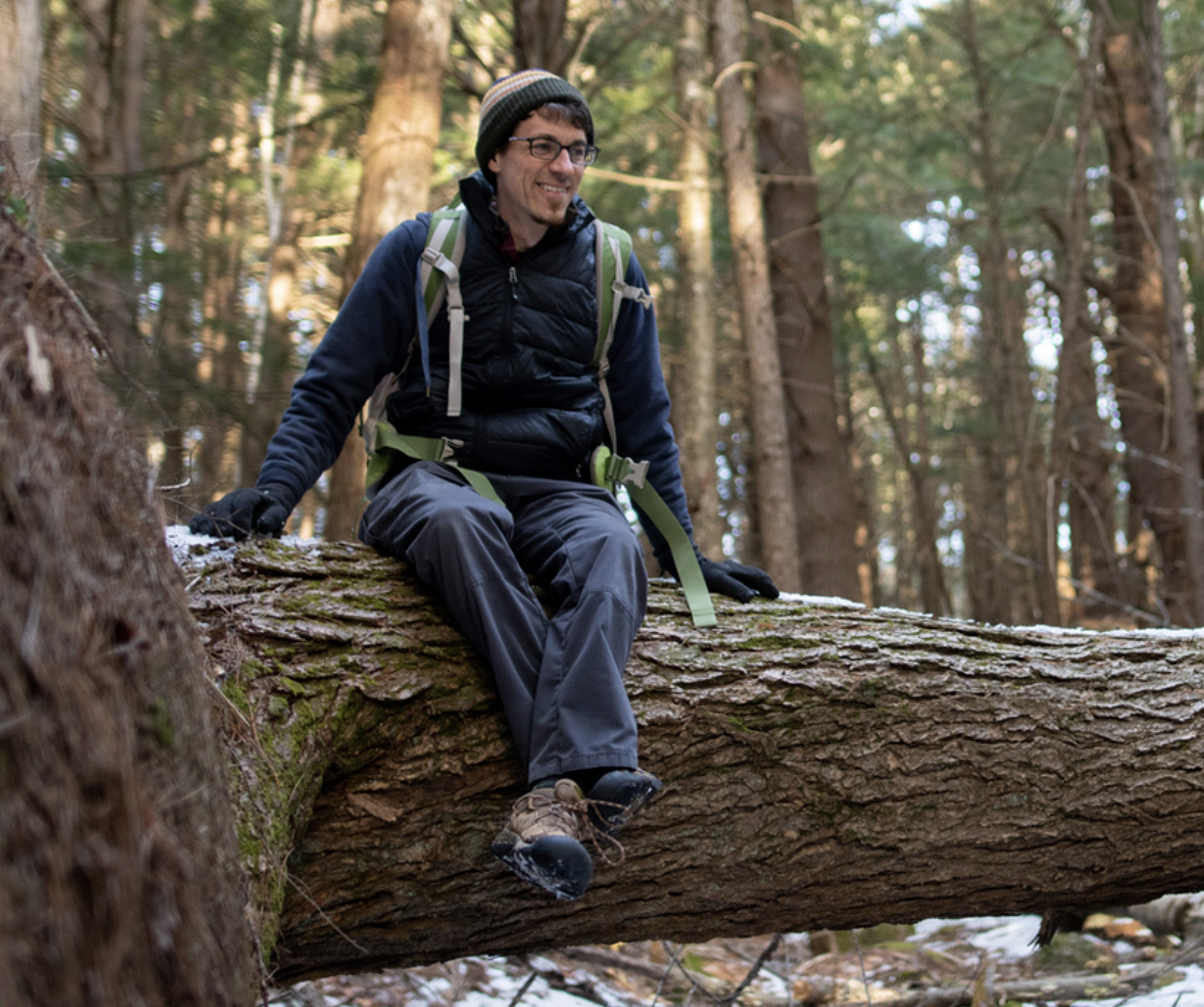 John Benjamin sits on a fallen tree in the forest. (photo © Ben Conant)